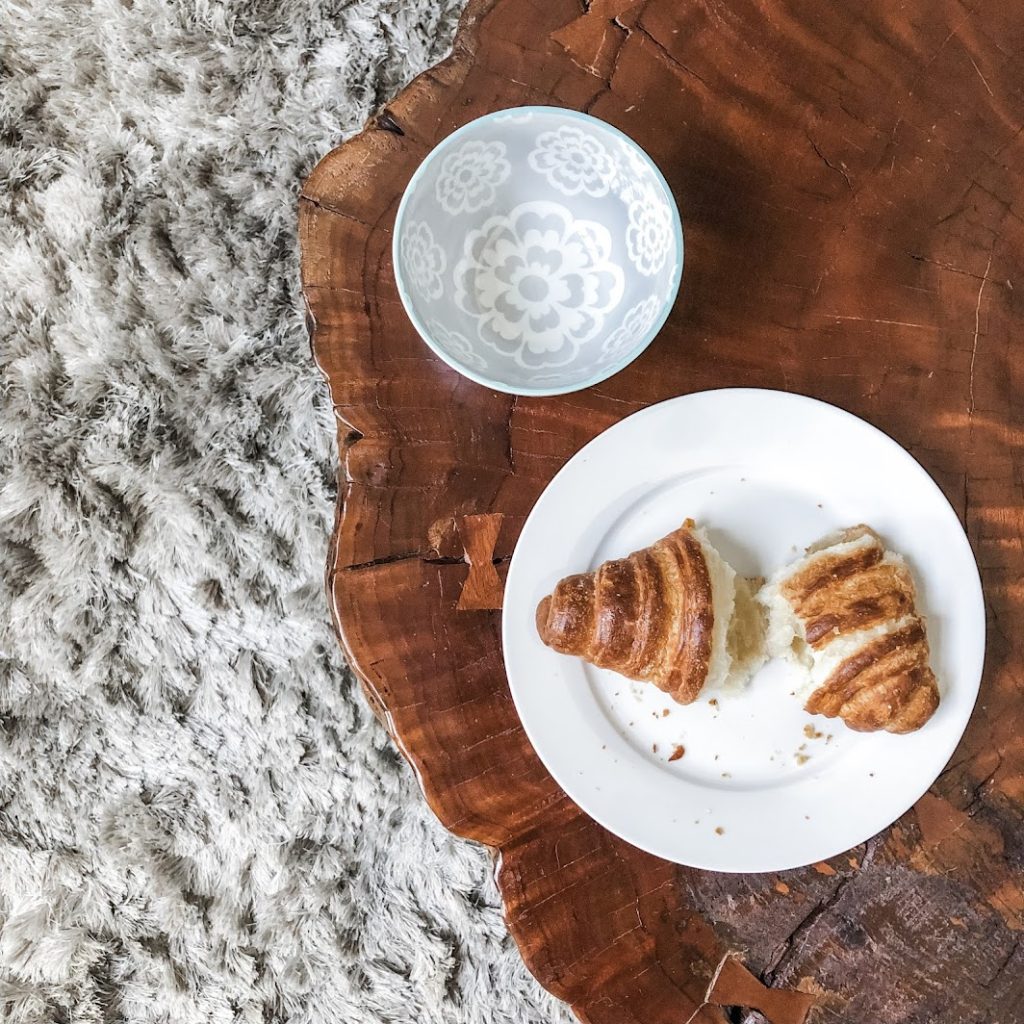 A croissant torn in half sitting on a white plate on top of a wooden table